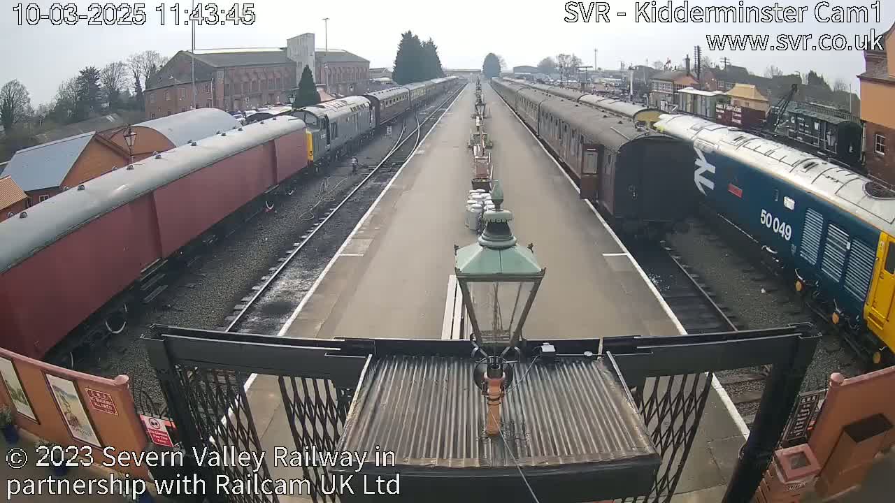 A train station on an overcast day with multiple passenger cars and locomotives on parallel tracks.