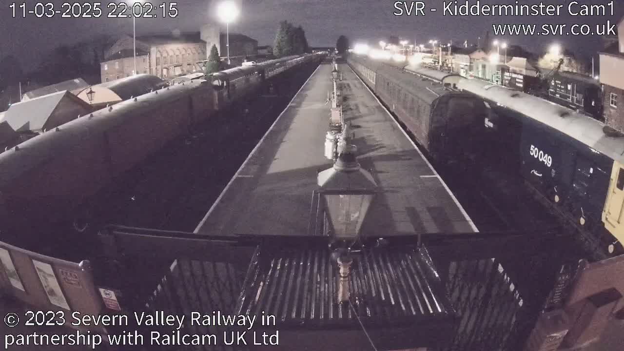 At night, long railway cars are parked on tracks extending into the distance under artificial lights.