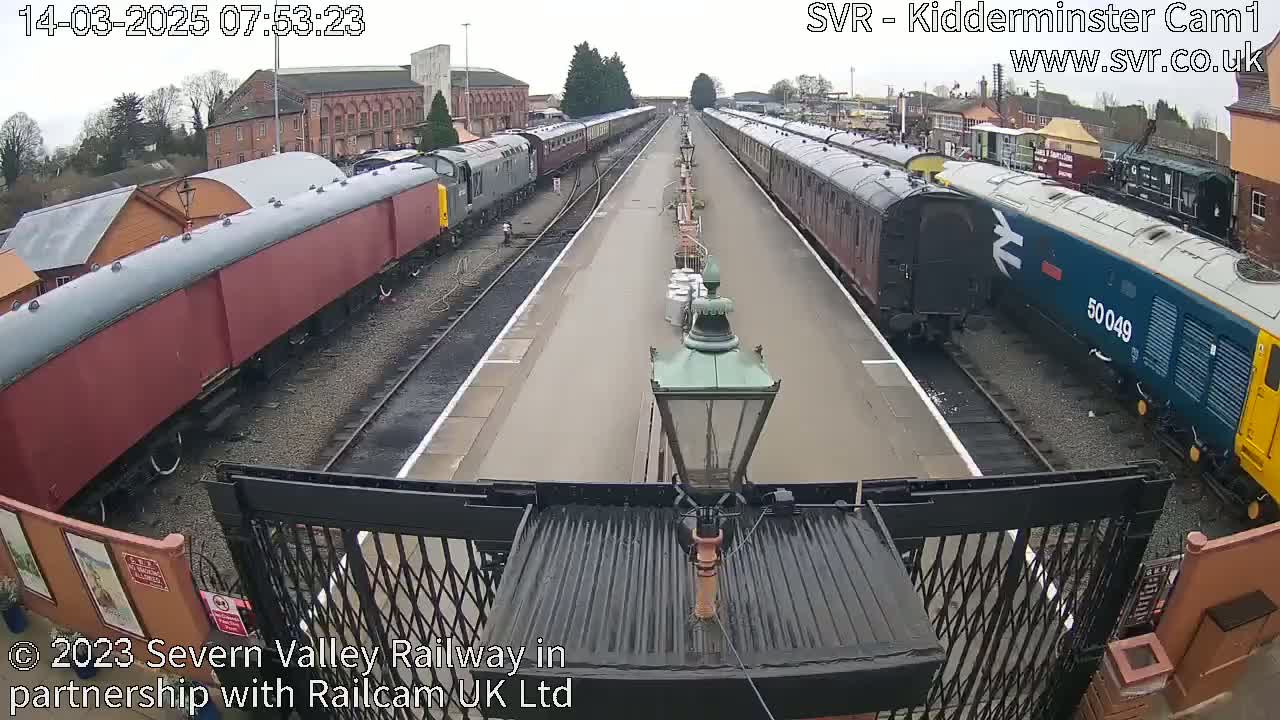 Several passenger train cars are parked on parallel railway tracks on an overcast day.