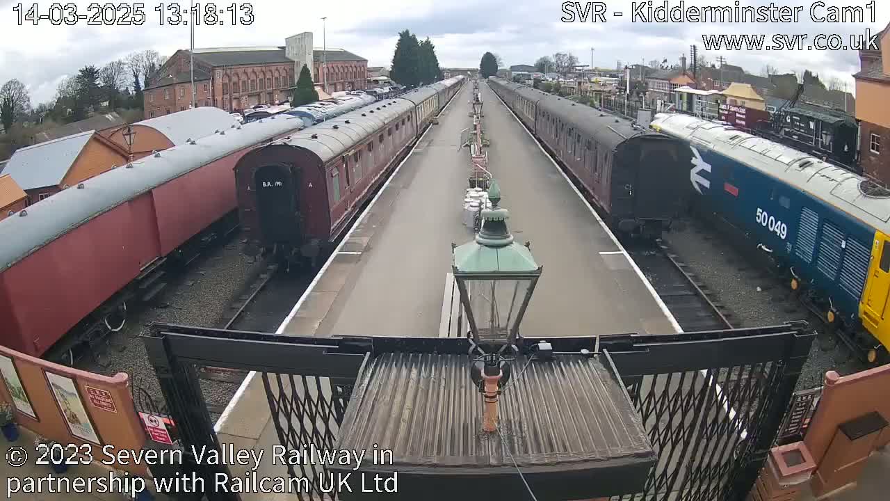 A train station platform with several railway carriages and a diesel locomotive under an overcast sky.