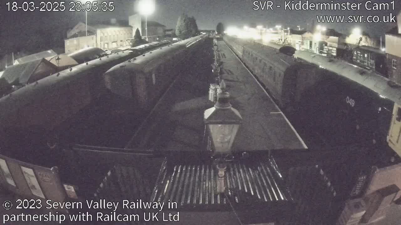 A nighttime view of several train cars parked on railway tracks, illuminated by artificial light.