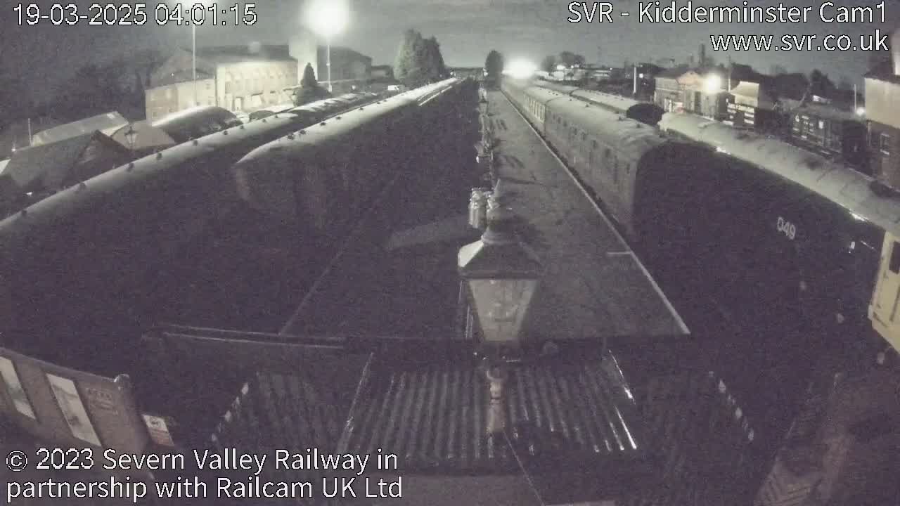 At night, several railway cars are parked in a station yard under dim lighting.