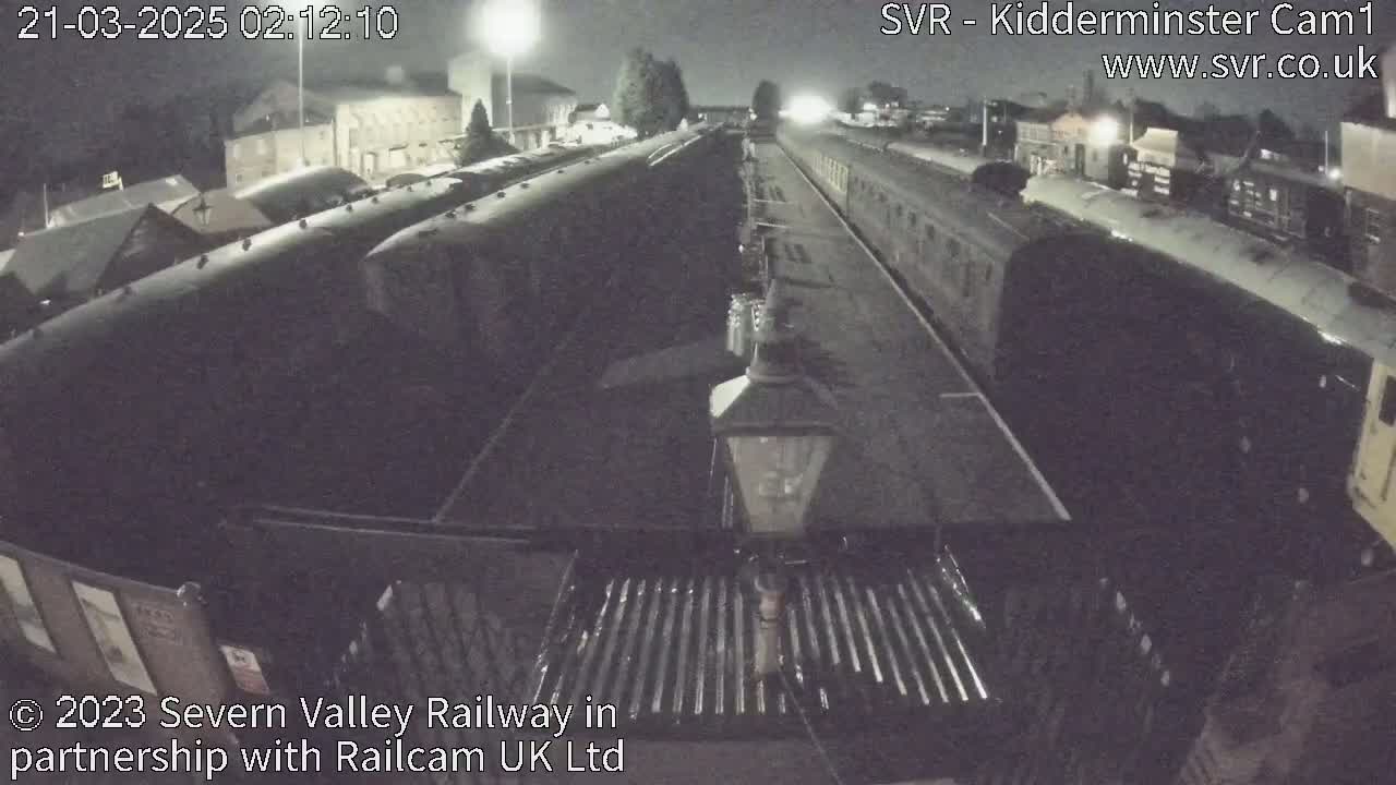 At night, several dark train cars are parked on a railway track next to a station platform.