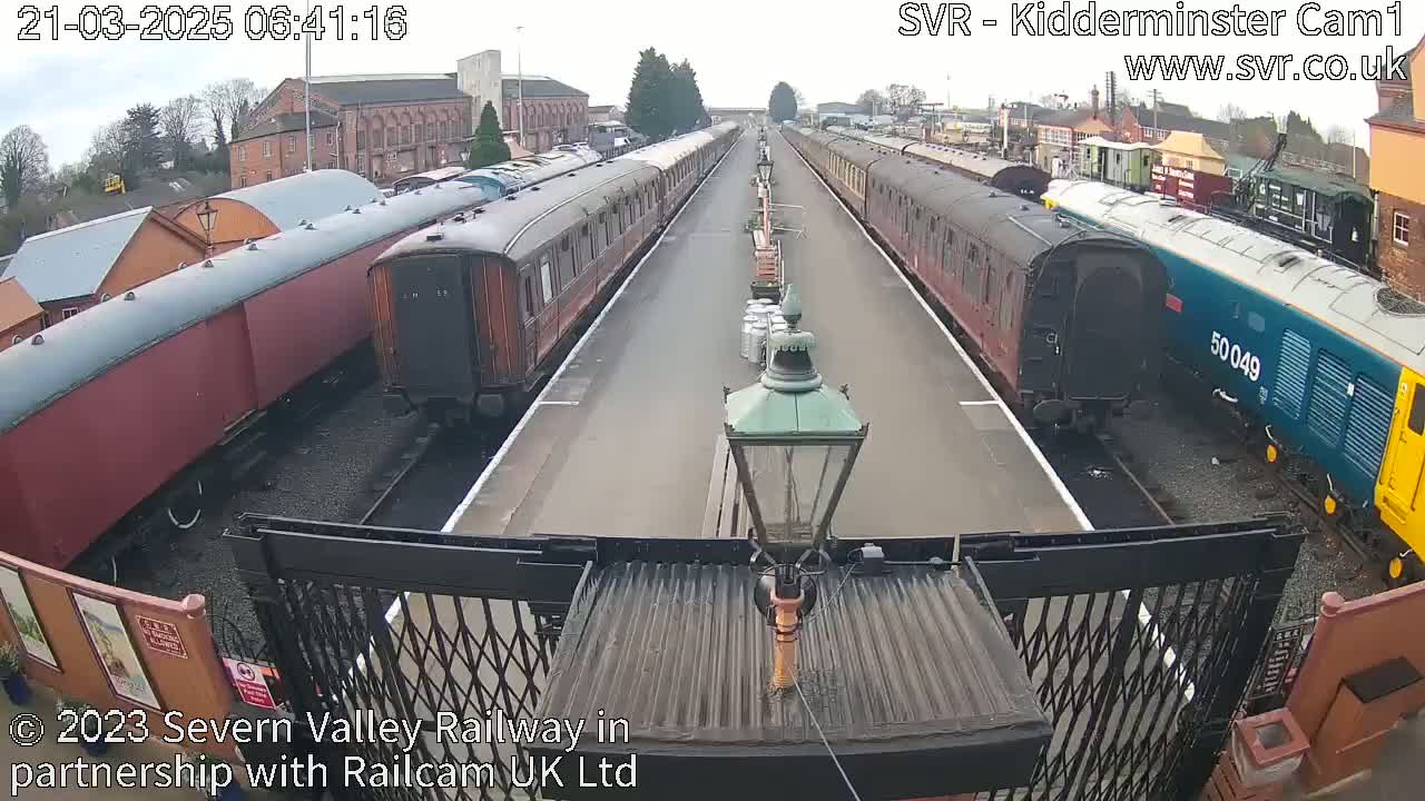 Two long lines of passenger train cars sit on parallel tracks on a clear day.