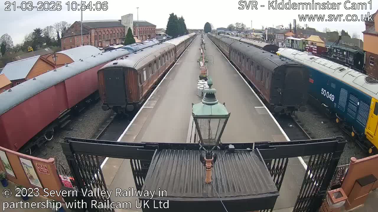 Two lines of passenger train cars sit on a railway track under a mostly cloudy sky.