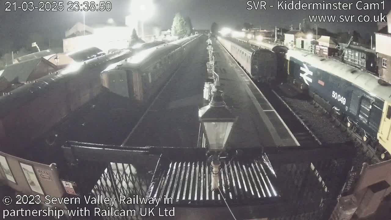 At night, two passenger trains are parked at a station platform under dim lighting.