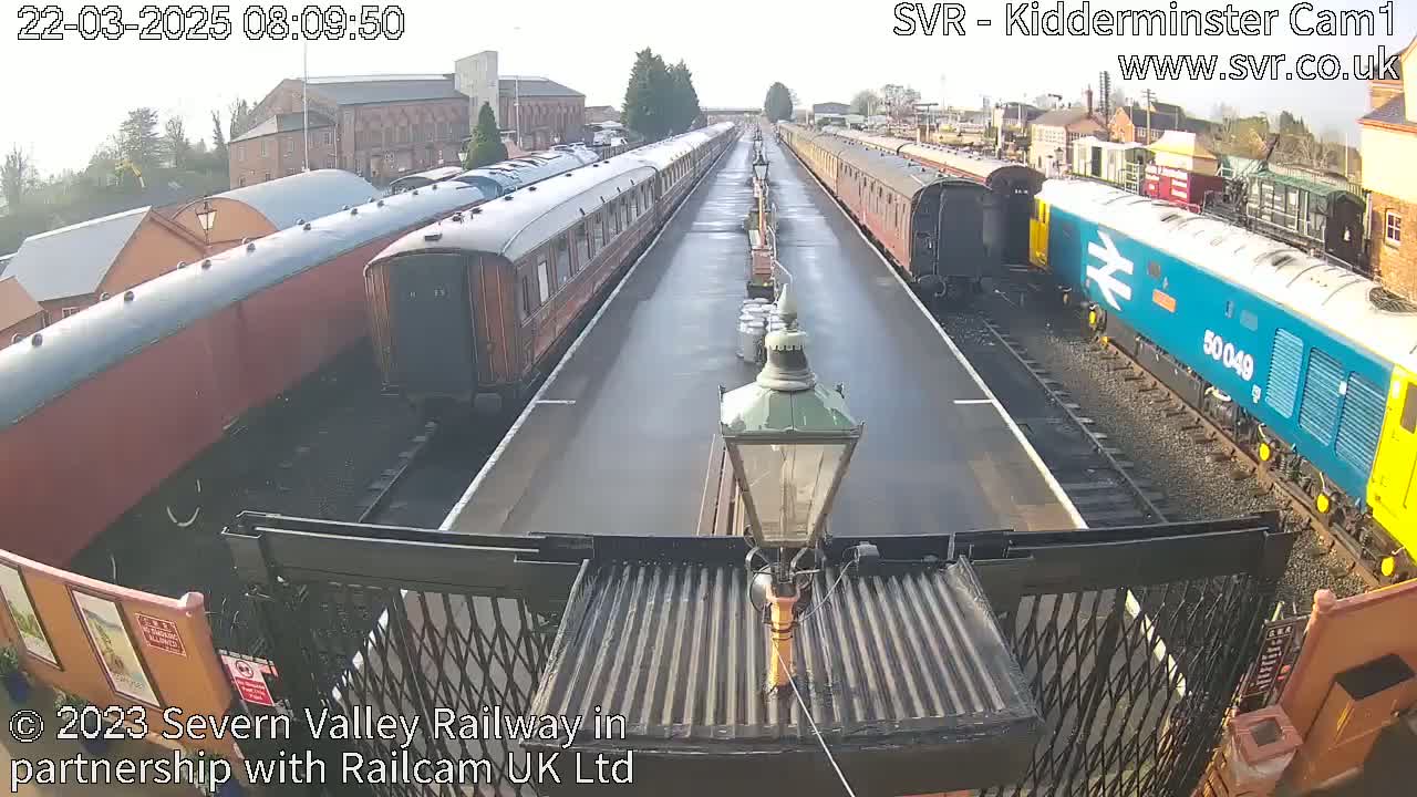 Two long lines of train cars are parked on a railway track on a mostly sunny day.