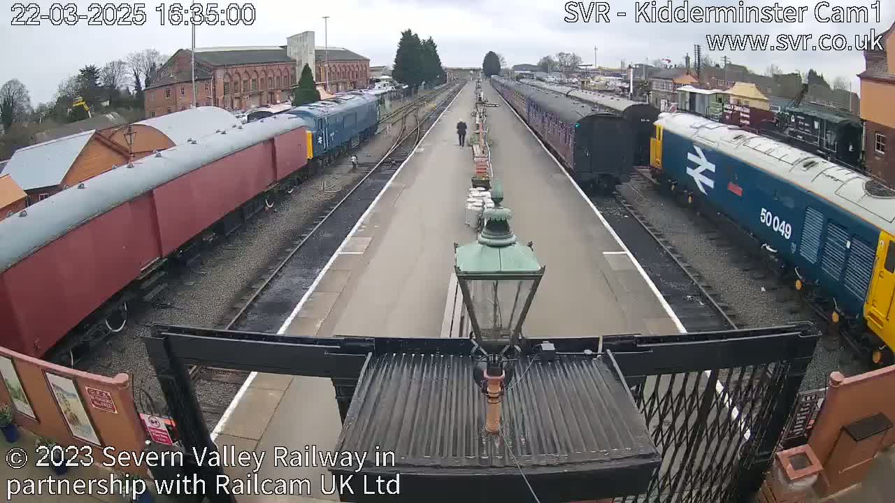 A person walks down a platform between two lines of stationary trains on an overcast day.