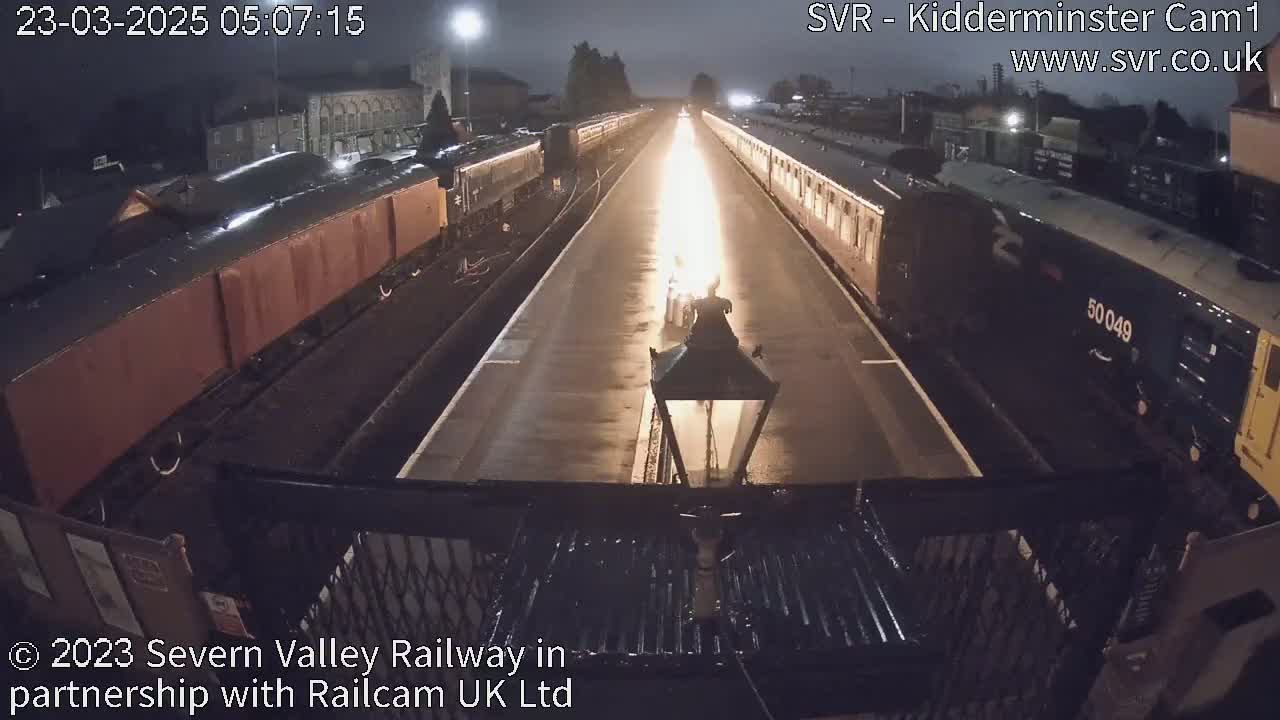 At night, two long trains face each other on parallel tracks with a bright light illuminating the area between them.