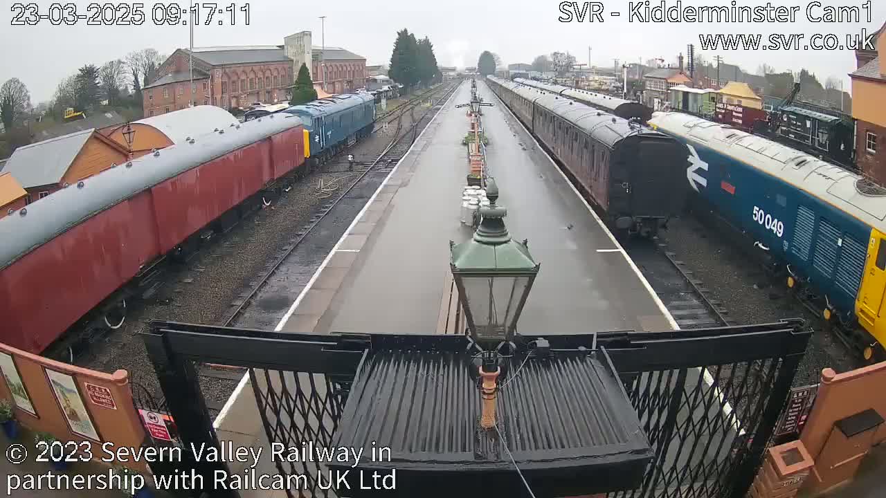 A wet railway station platform with two long passenger trains parked on either side.
