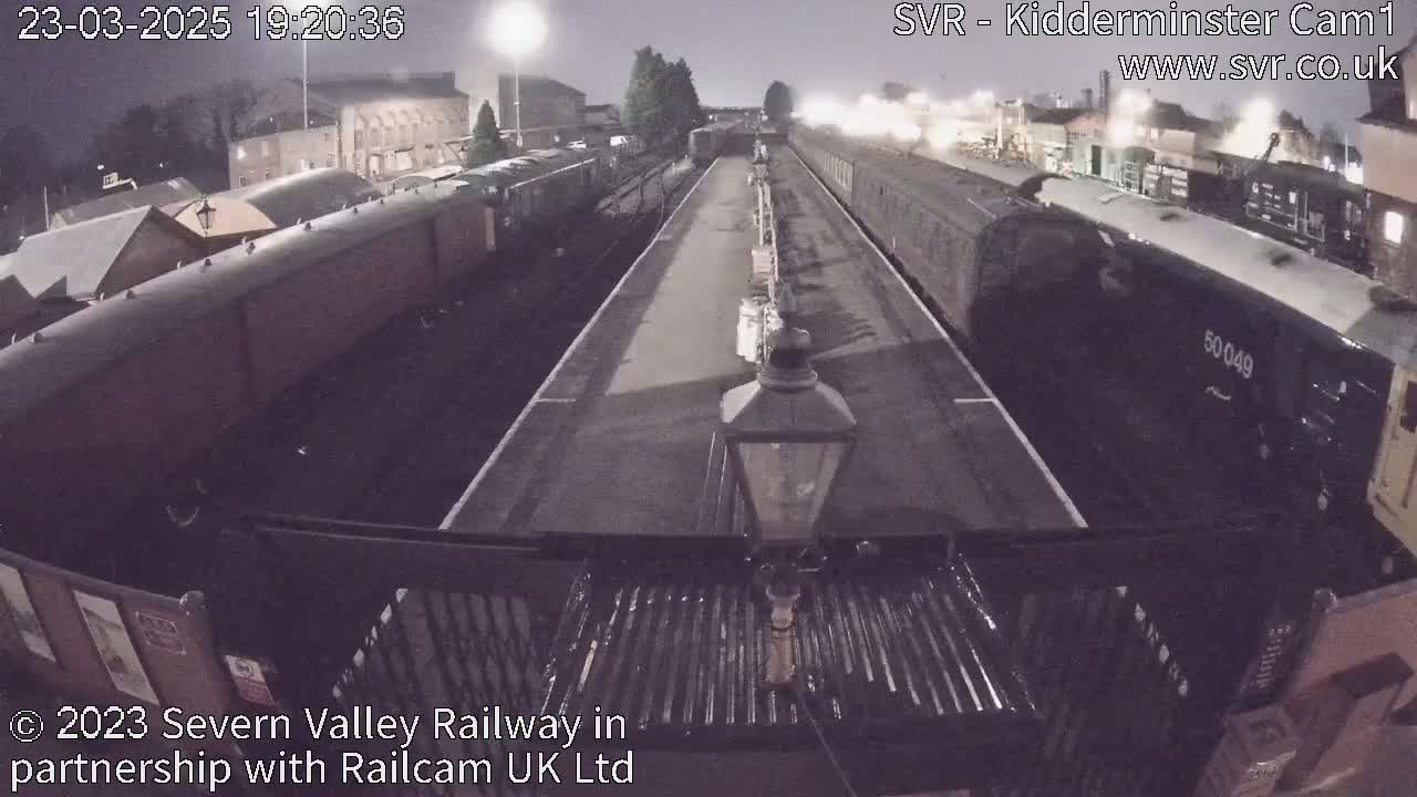 At night, several railway carriages are parked at a station platform under dim lighting.