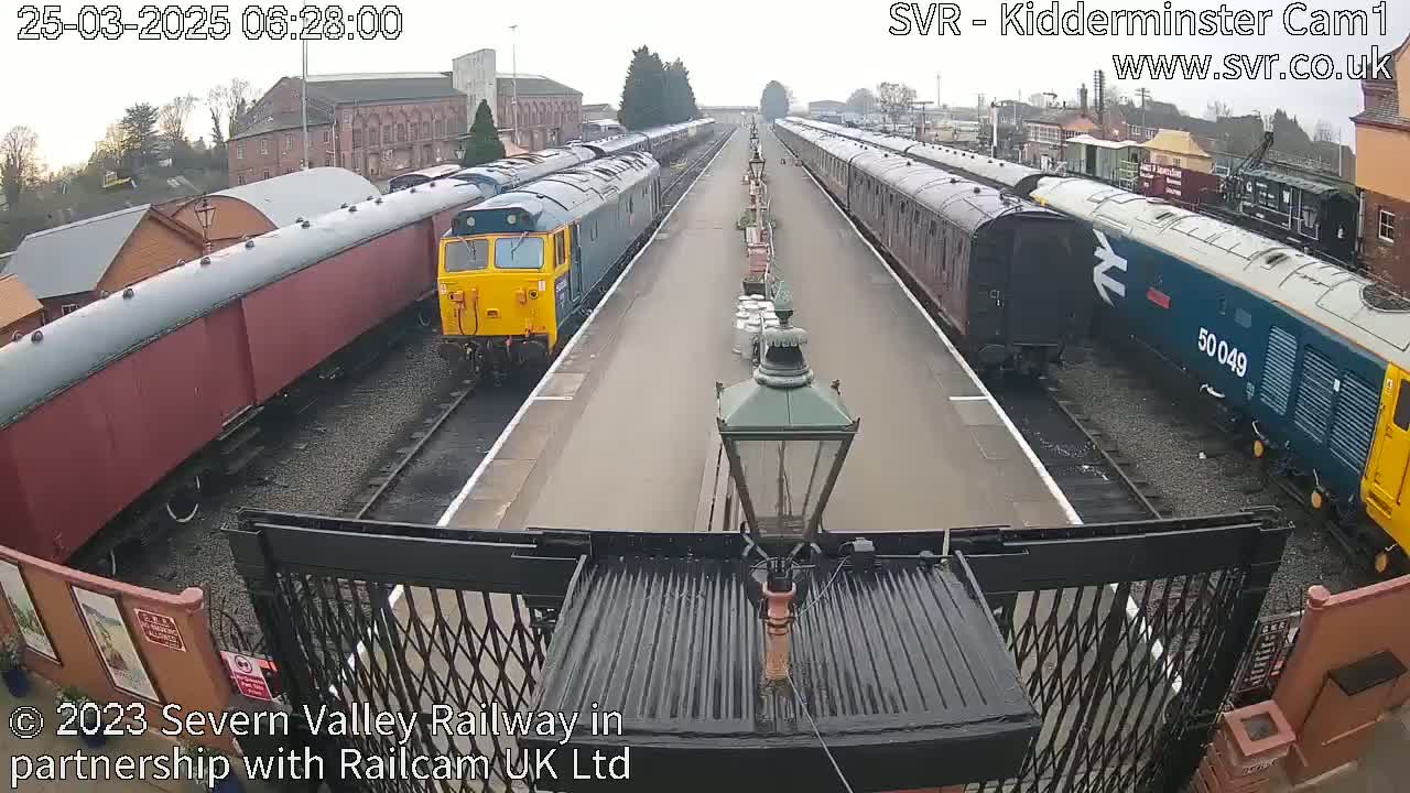 A train station on an overcast day with multiple passenger cars and locomotives on parallel tracks.