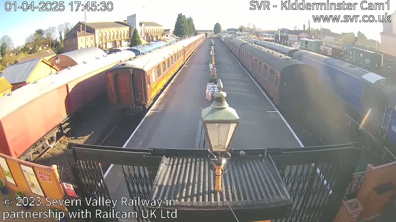 Two long lines of passenger train cars sit on a sunny railway platform.