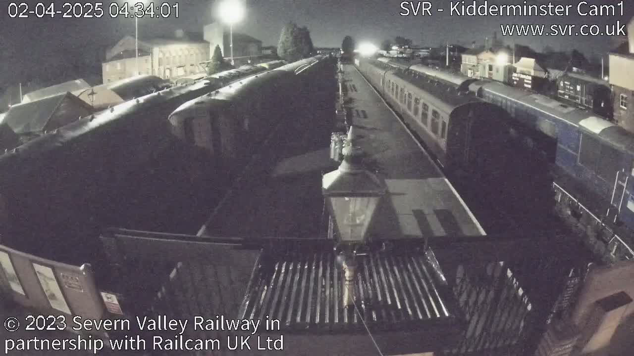 A nighttime view of a train station platform with multiple passenger trains parked alongside it under dark skies.