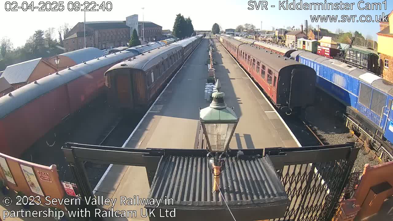 Several passenger train cars are parked on a sunny day at a railway station.