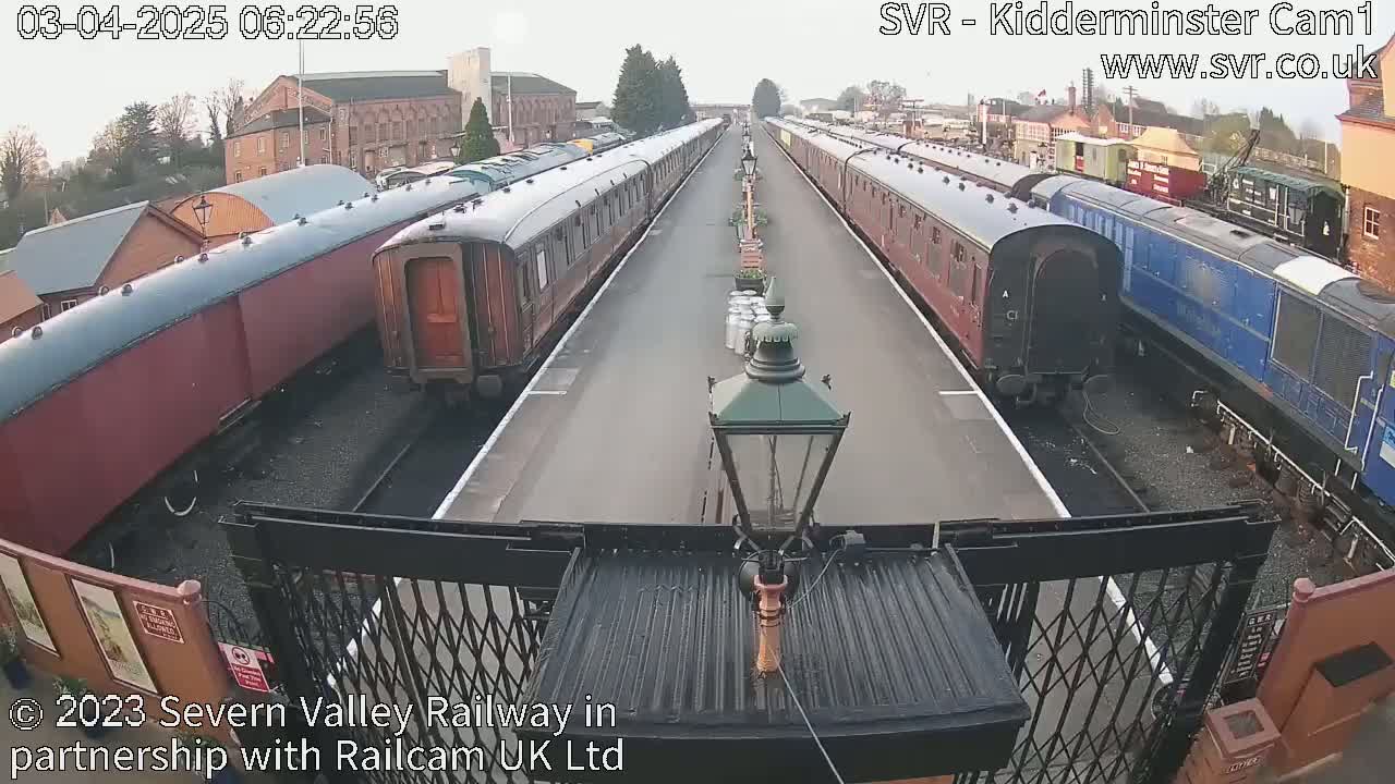 Two long passenger trains are parked on parallel tracks at a station on an overcast day.