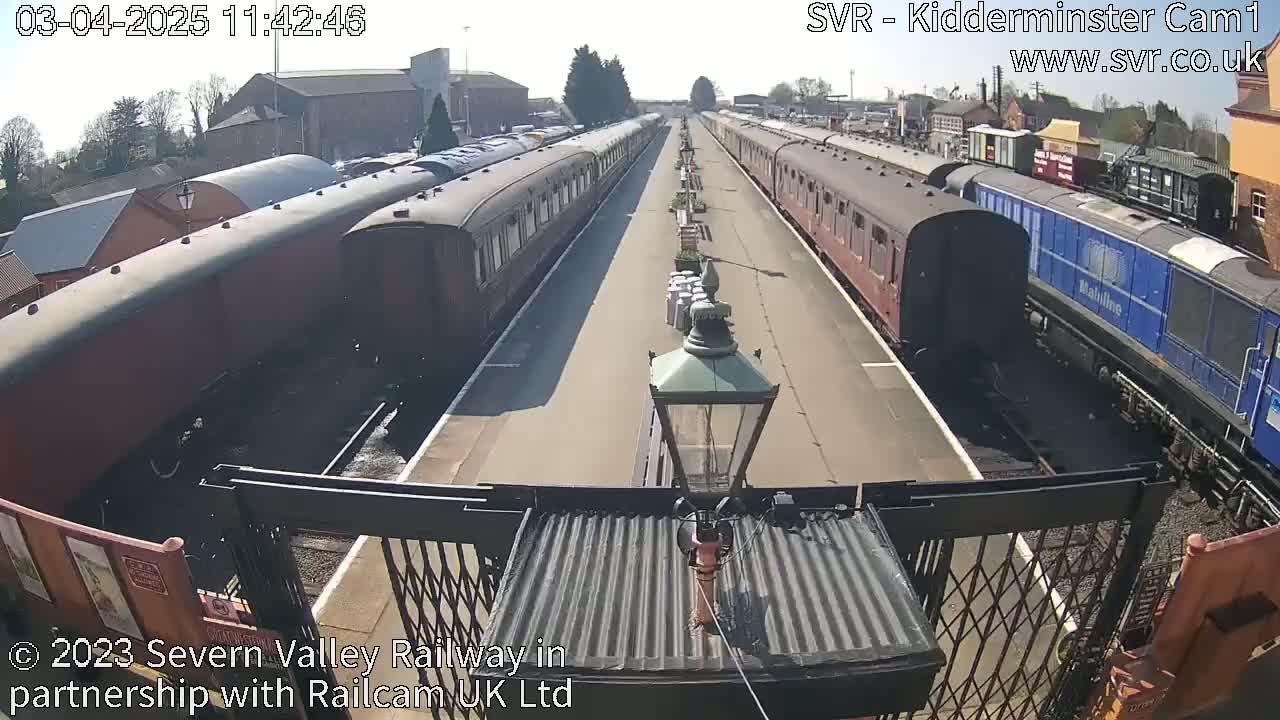A sunny day at a train station shows multiple train cars on parallel tracks.
