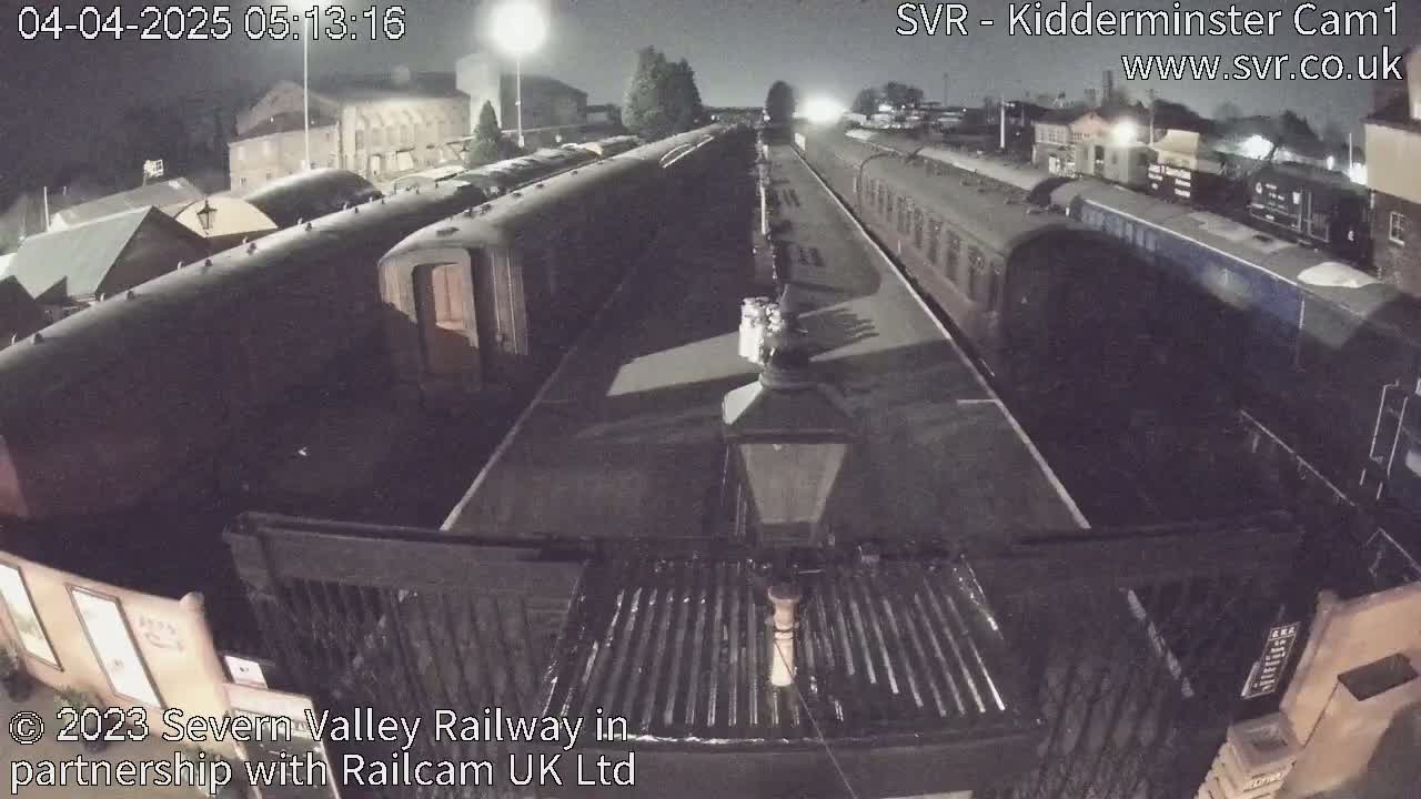 At night, several dark passenger train cars are parked at a station platform.