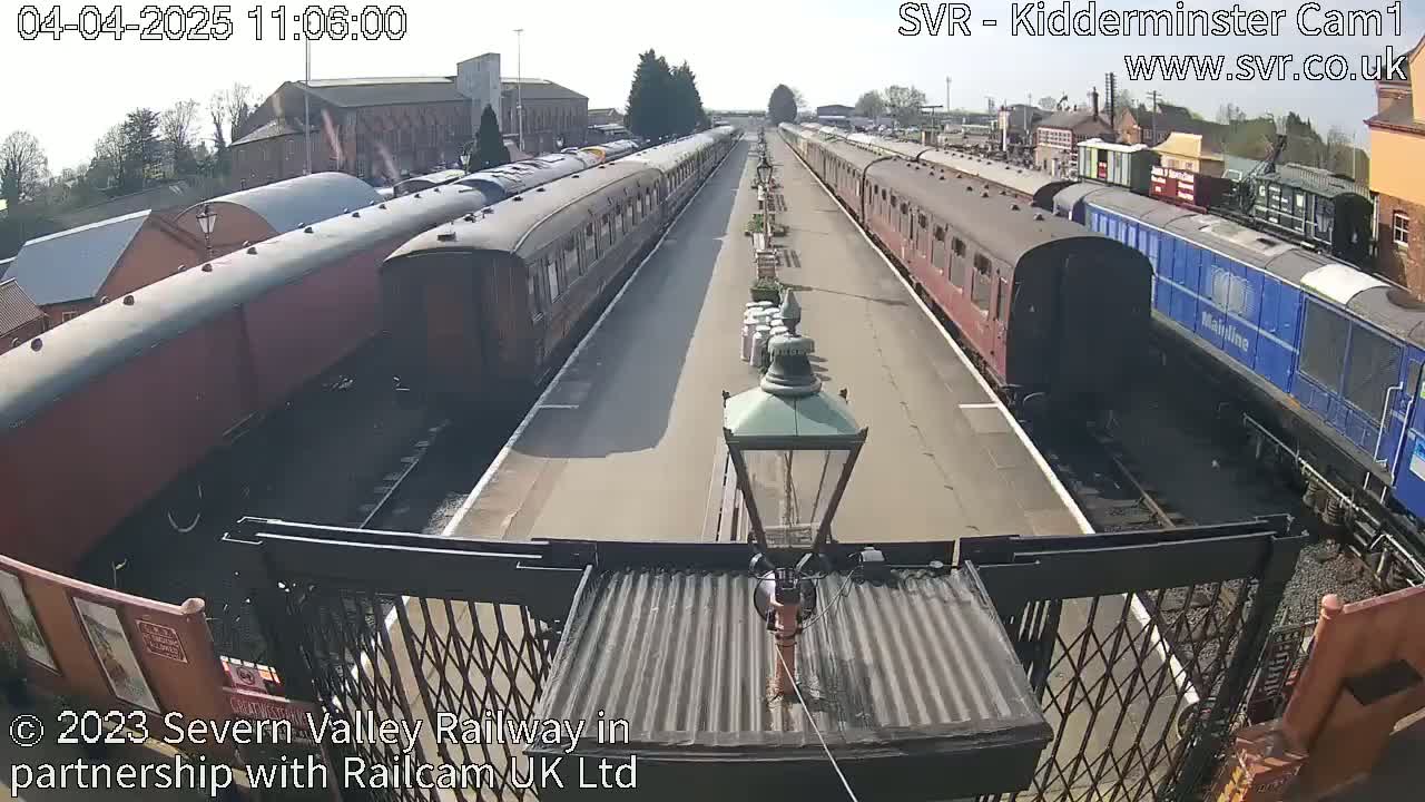 Two long trains of passenger cars sit at a station platform on a sunny day.