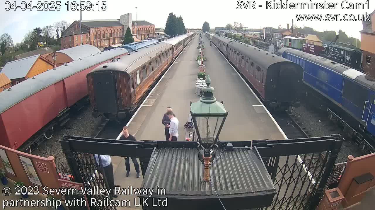 A high-angle view shows two lines of vintage train cars parked at a station on a partly sunny day.