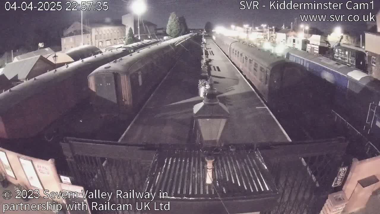 A nighttime view of several passenger train cars parked at a station platform under dark skies.
