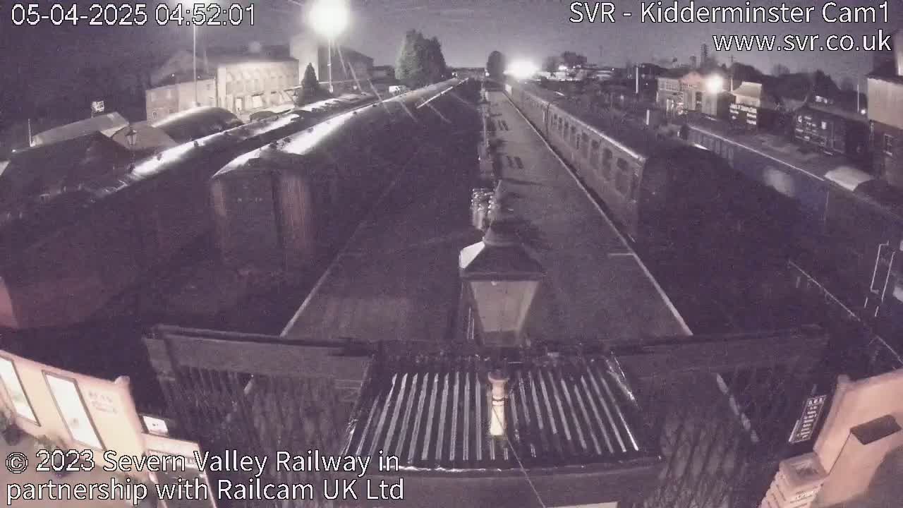 A nighttime view of a train station platform with several train cars parked on the tracks under dim lighting.