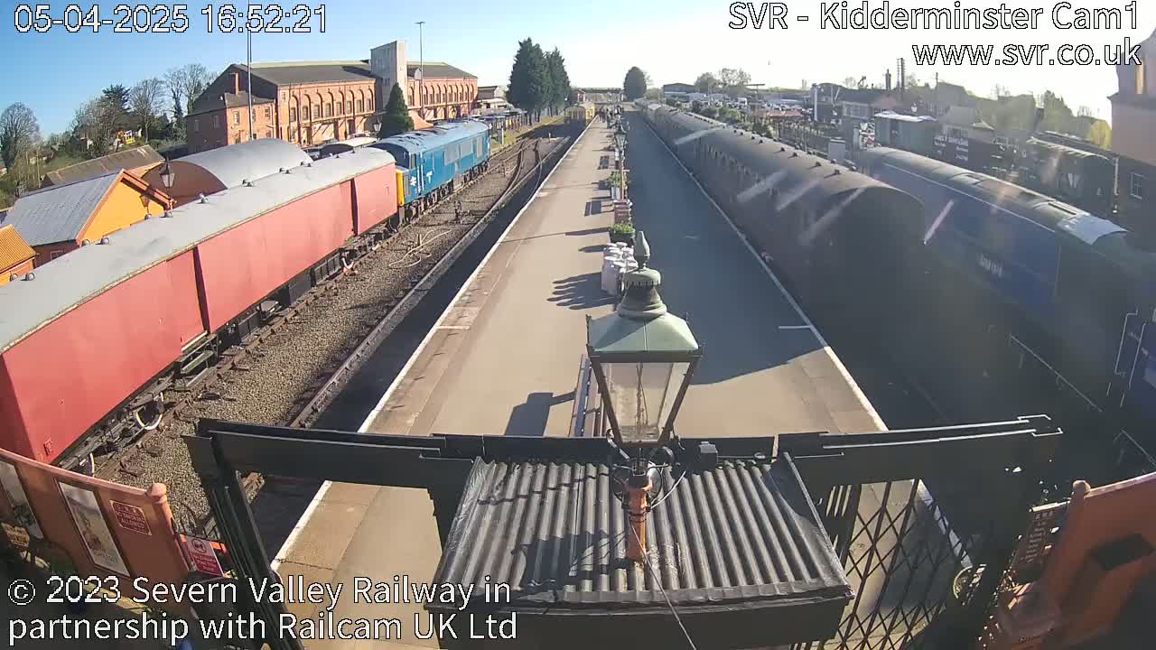 A sunny view of a train station with several passenger cars and locomotives on the tracks.