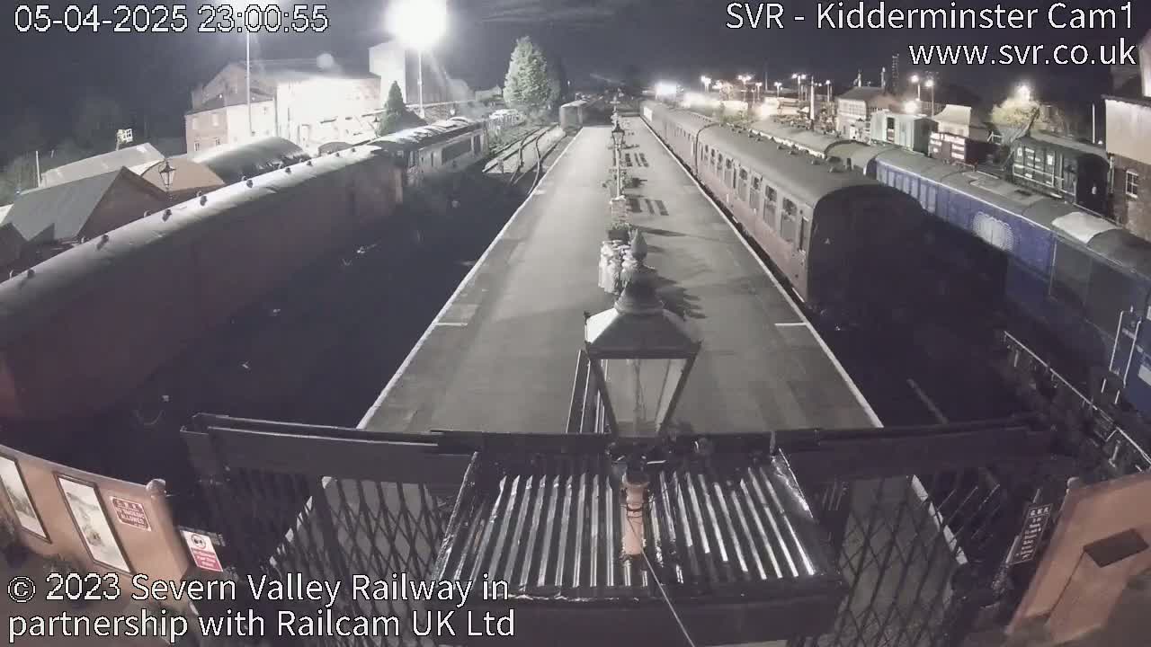At night, two long trains are parked on either side of a platform at a train station.