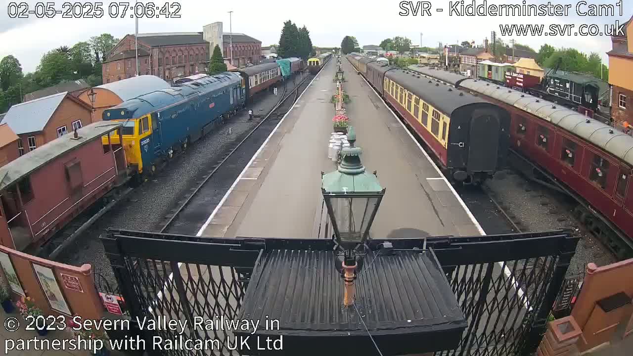 A train station on an overcast day with several passenger cars and locomotives parked on parallel tracks.