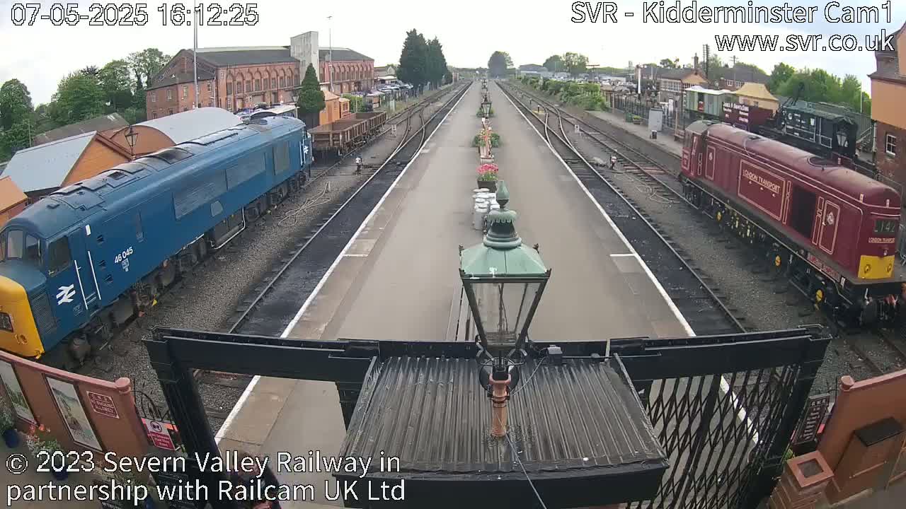 Two diesel locomotives are parked on either side of a railway platform on an overcast day.