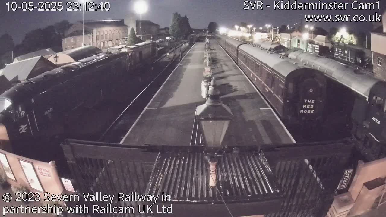 At night, two trains are parked on a platform at a station.