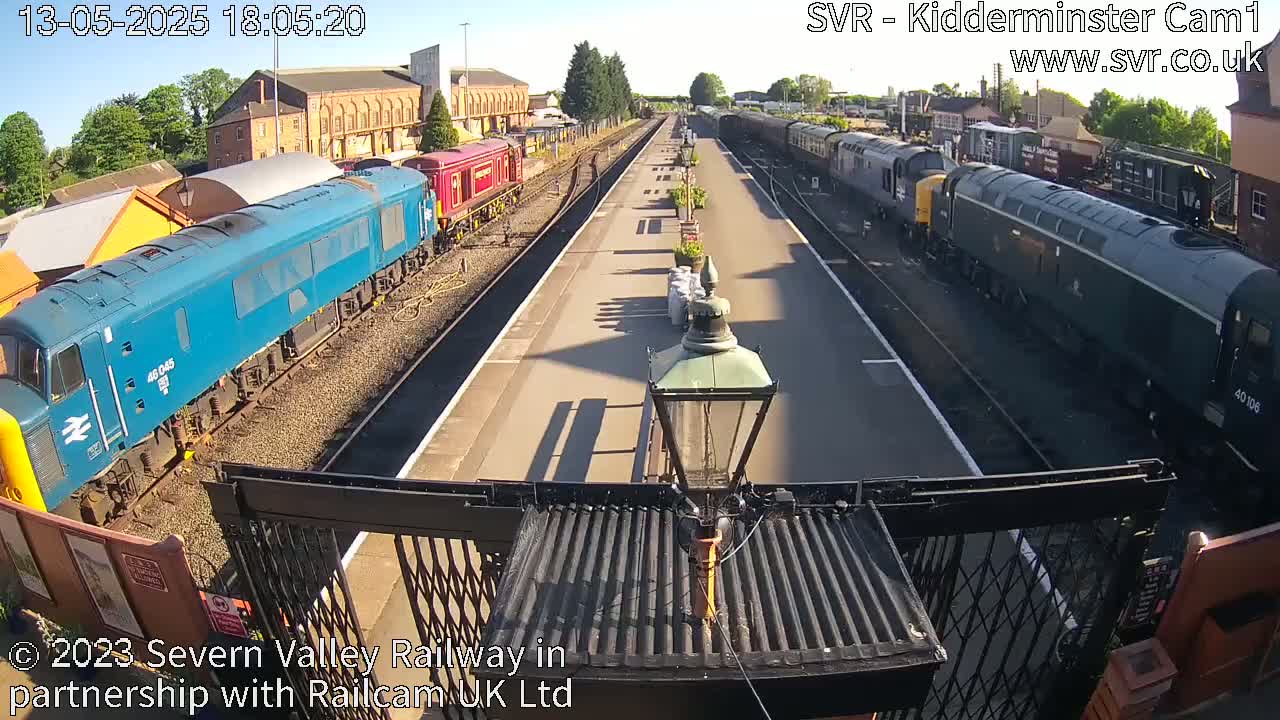 A sunny view of a railway station platform with multiple trains parked on either side.