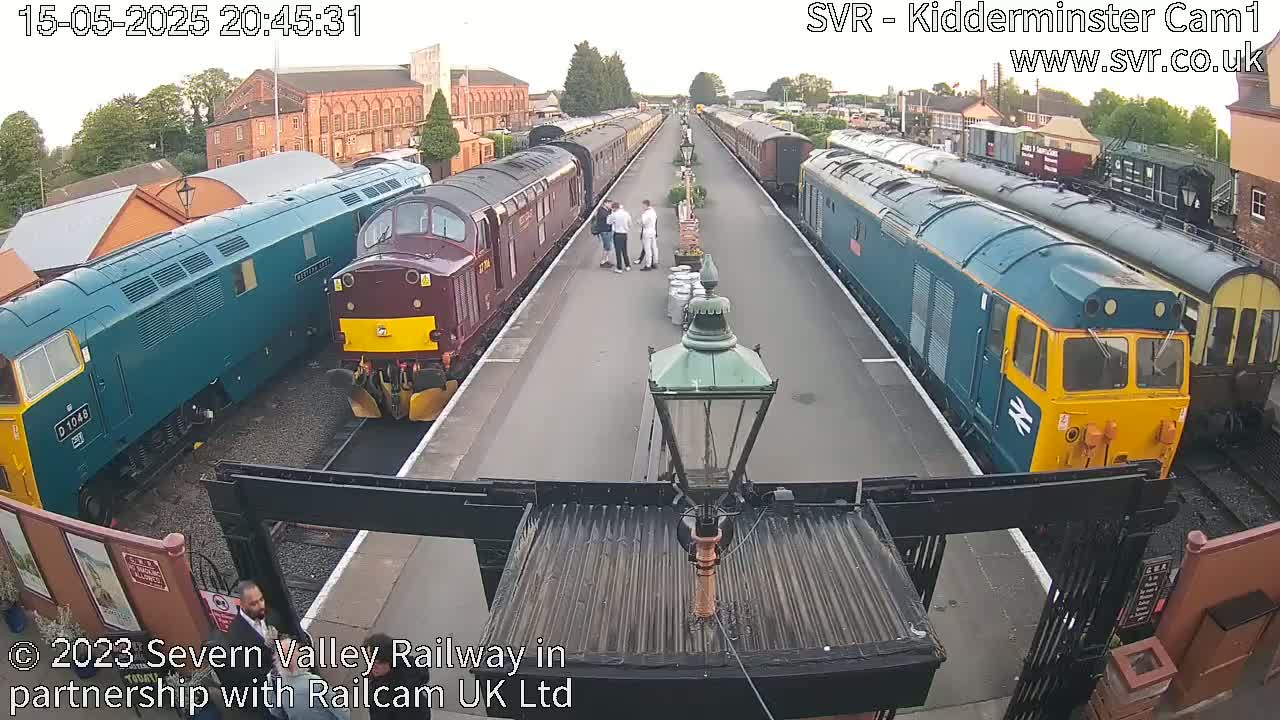 Several diesel locomotives and passenger cars are parked on a railway platform in the evening.