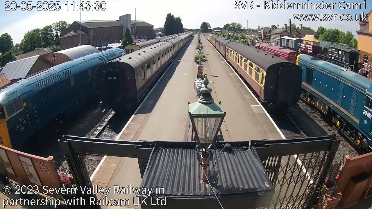 Two long passenger trains are parked at a station on a sunny day.