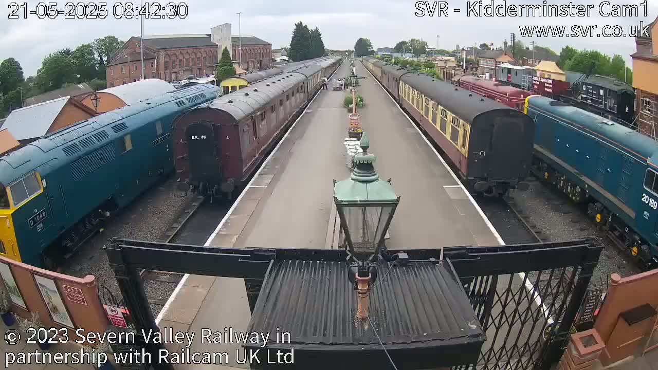 A railway station platform on an overcast day with several passenger train cars and locomotives parked on parallel tracks.