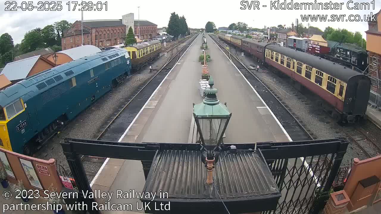 A view of a railway station platform with several locomotives and passenger cars on the tracks on an overcast day.