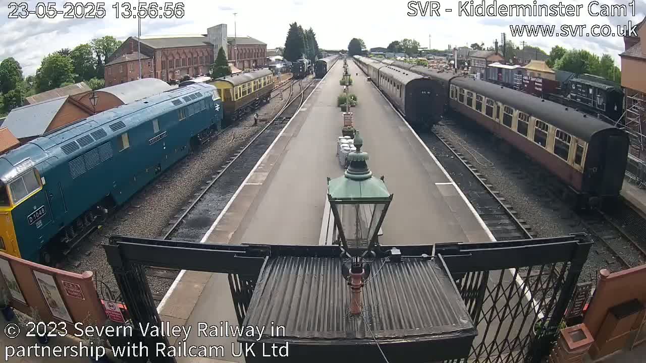 A railway station platform on a sunny day with several passenger trains and a diesel locomotive.