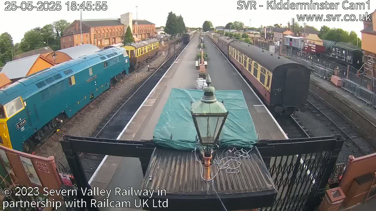 A train station with two trains on separate tracks under a partly cloudy sky.