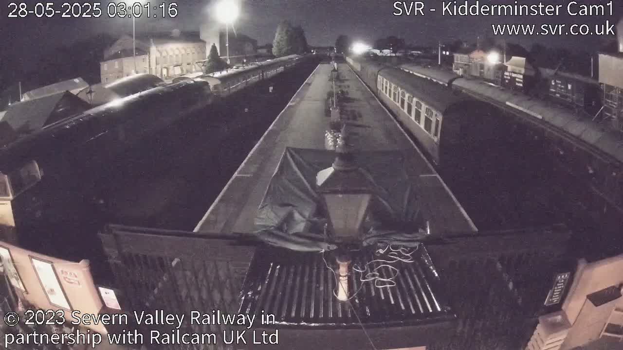 A nighttime view from a low vantage point shows several railway cars parked on tracks at a station.
