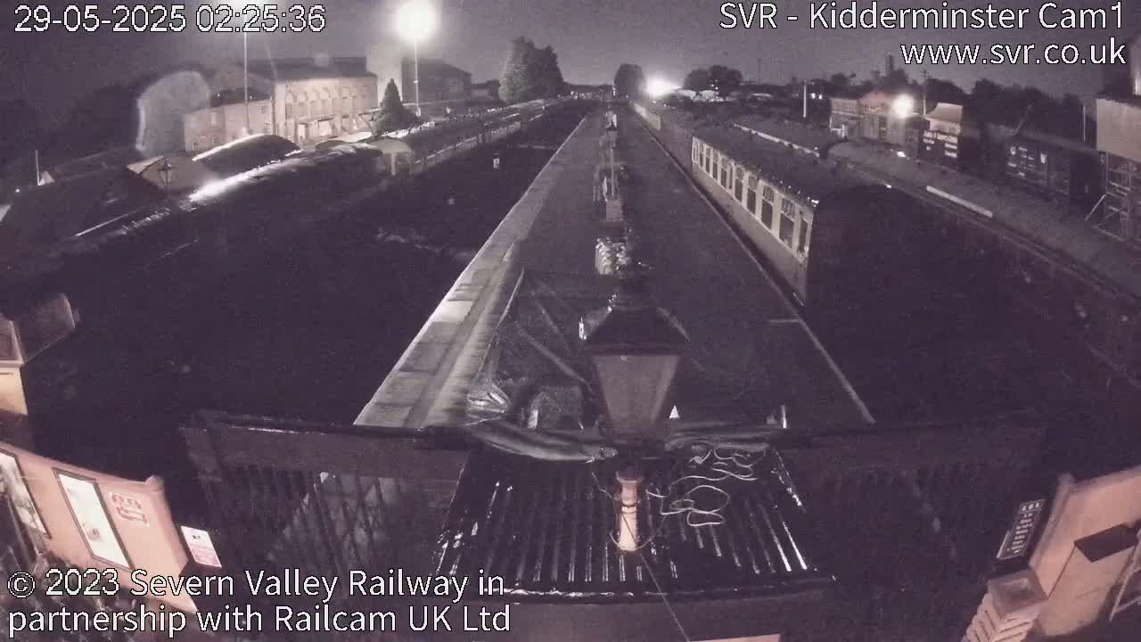 A nighttime view from a train of a railway station with several train cars parked along the tracks.