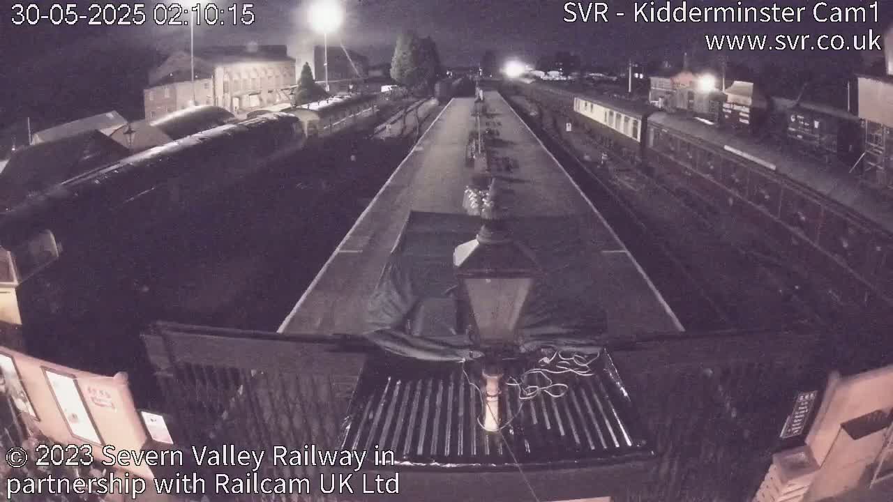 A nighttime view from atop a train shows a railway yard with multiple train cars parked along tracks under artificial light.