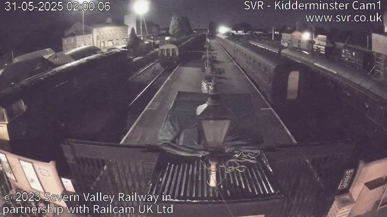 At night, several dark train cars are parked on a railway track.