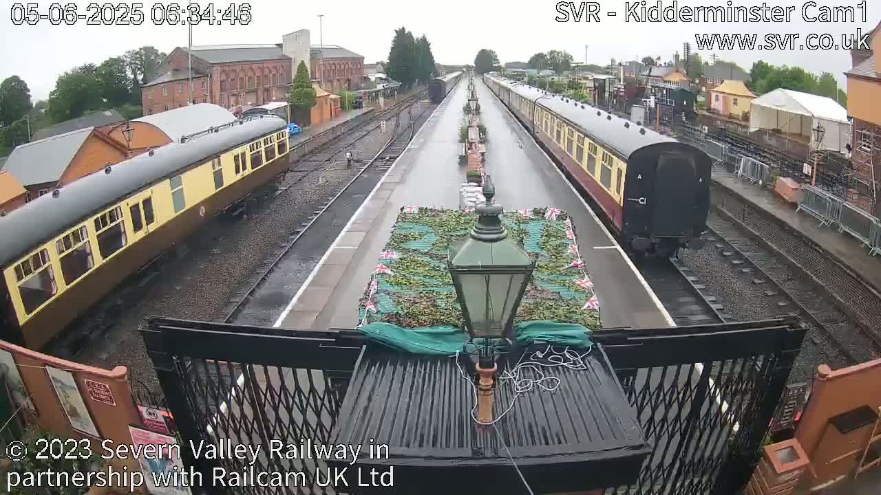 Two vintage passenger trains are parked at a railway station on a rainy day.