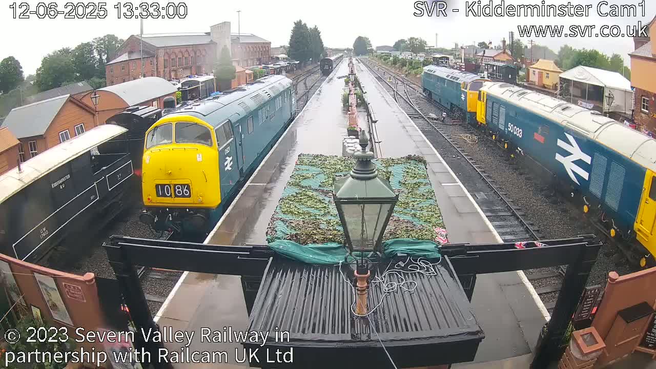 Several diesel locomotives are parked at a railway station in the rain.
