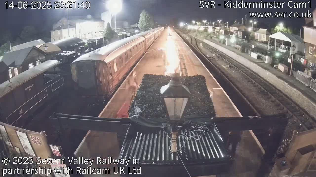 A train pulls into a railway station where several people are gathered, under an overcast sky.