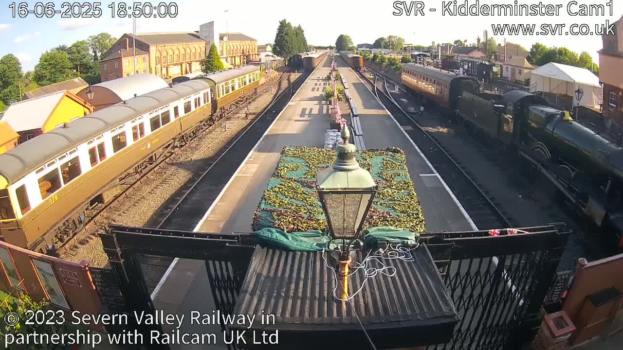 A sunny view of a railway station with passenger cars and a steam locomotive on the tracks.