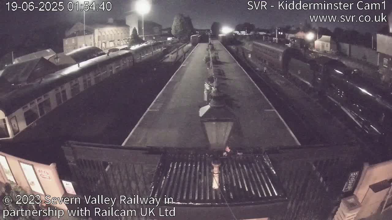 A nighttime, overhead view of a train station platform with several passenger cars and a locomotive parked on the tracks.
