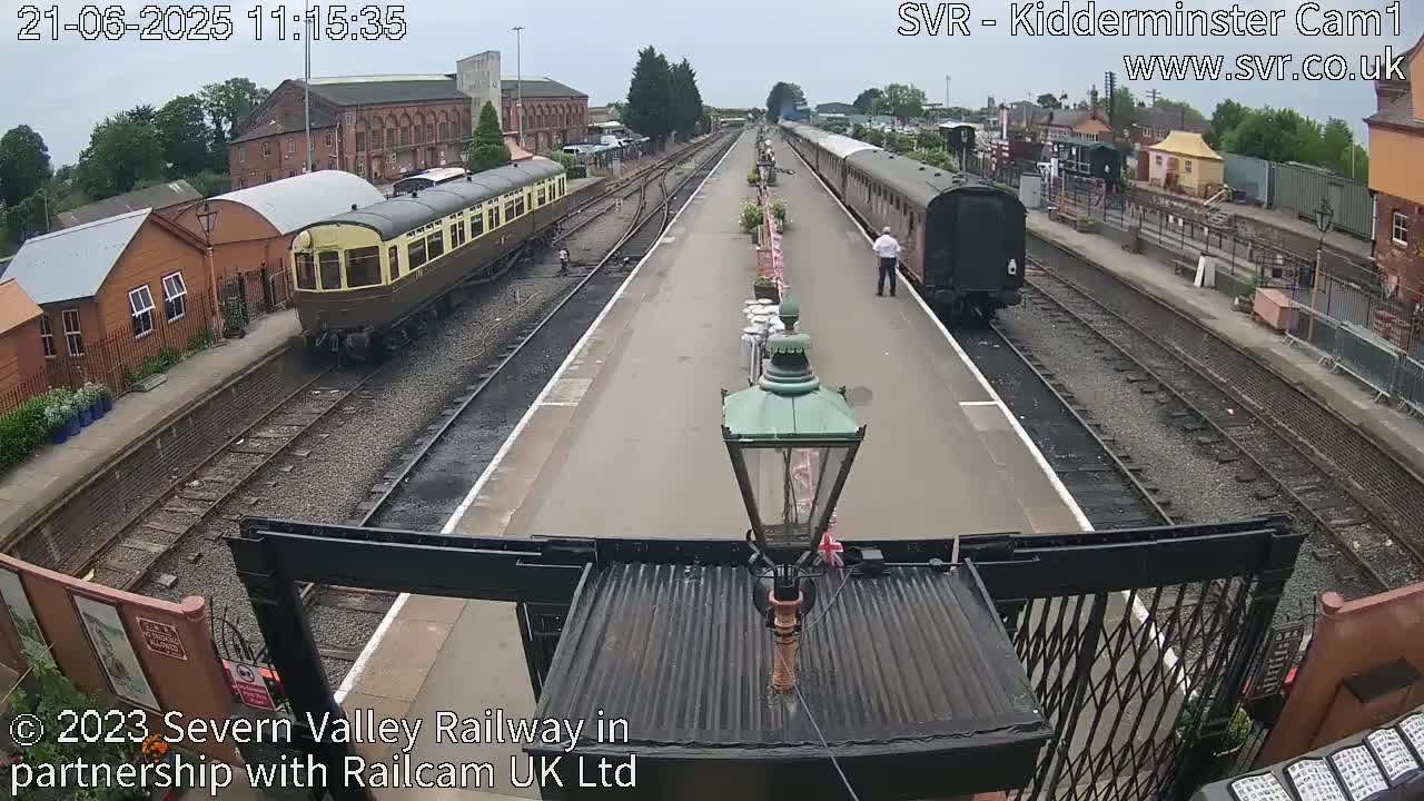 Two passenger trains are at a station on a partly cloudy day.