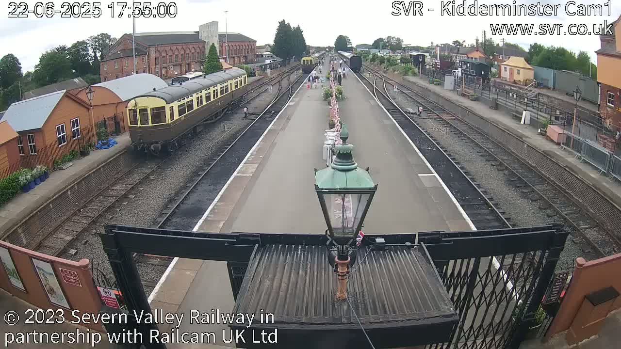 A railway station platform with a vintage train arriving, under partly cloudy skies.