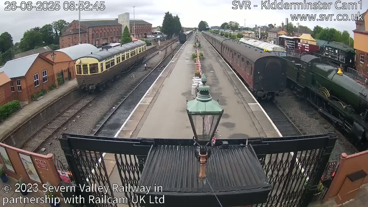 Several passenger train cars and a steam locomotive are parked at a train station on an overcast day.
